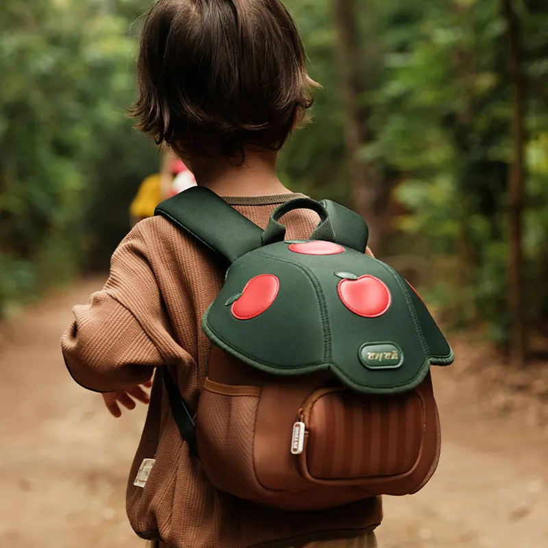 Dziecko w brązowym swetrze idące przez las z plecakiem ZOY ZOII Jabłko na plecach.