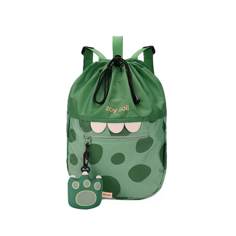 Zielony plecak dziecięcy Zoy Zoii z motywem dinozaura, charakterystycznymi białymi zębami, ciemnymi plamami oraz brelokiem w kształcie łapy.